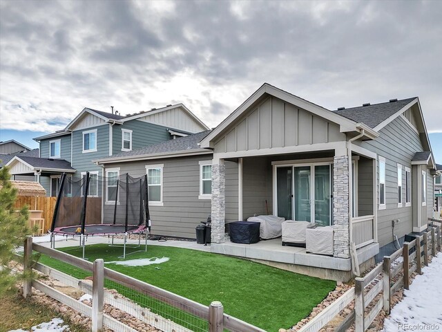 back of house featuring a lawn, a trampoline, fence, roof with shingles, and board and batten siding