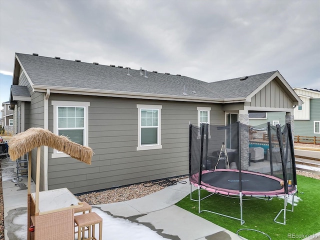 rear view of house featuring a lawn, board and batten siding, a trampoline, and roof with shingles