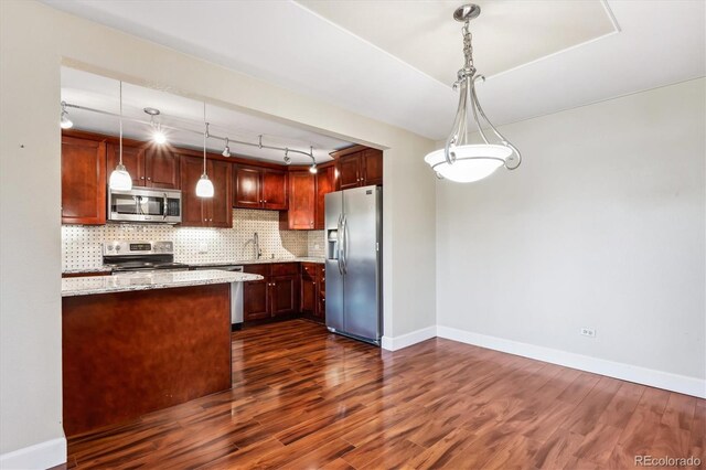 kitchen featuring light stone counters, pendant lighting, dark wood-type flooring, appliances with stainless steel finishes, and decorative backsplash