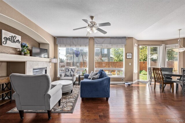 living room with a tiled fireplace, a textured ceiling, baseboards, ceiling fan, and hardwood / wood-style flooring