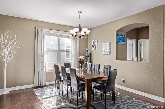 dining space with arched walkways, baseboards, a chandelier, and wood finished floors