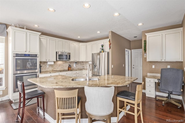 kitchen featuring sink, a kitchen island with sink, white cabinetry, appliances with stainless steel finishes, and dark hardwood / wood-style flooring