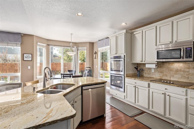 kitchen with appliances with stainless steel finishes, light stone counters, decorative light fixtures, dark hardwood / wood-style floors, and sink