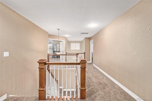 hallway featuring an upstairs landing, visible vents, a textured wall, carpet floors, and baseboards