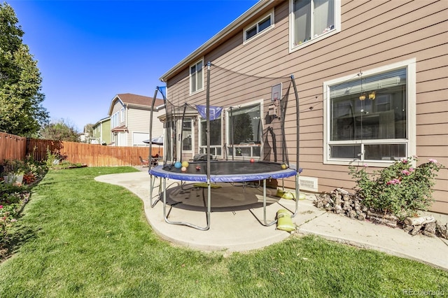 back of house featuring a lawn, a trampoline, a patio, and fence