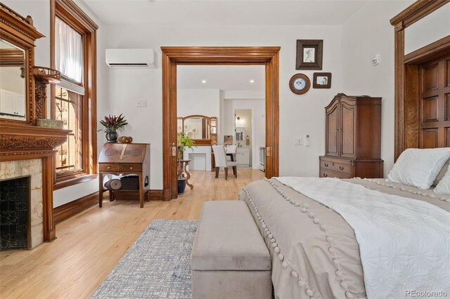 bedroom with a tiled fireplace, light wood-style flooring, multiple windows, and a wall unit AC