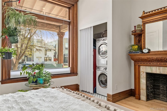 clothes washing area with baseboards, stacked washing maching and dryer, wood finished floors, a fireplace, and laundry area