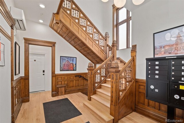 foyer with stairway, a wainscoted wall, light wood finished floors, and a wall unit AC