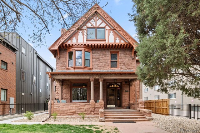 view of front facade with a porch, stone siding, and fence