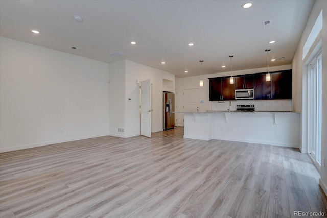 kitchen with hanging light fixtures, light wood-type flooring, light stone countertops, dark brown cabinetry, and stainless steel appliances