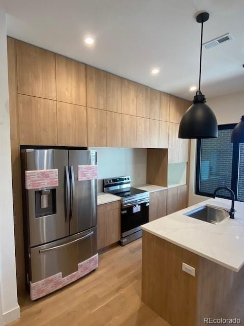 kitchen with pendant lighting, sink, stainless steel appliances, and light wood-type flooring