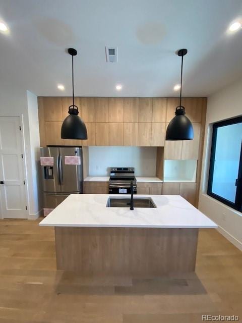 kitchen featuring a sink, hanging light fixtures, appliances with stainless steel finishes, modern cabinets, and a center island with sink