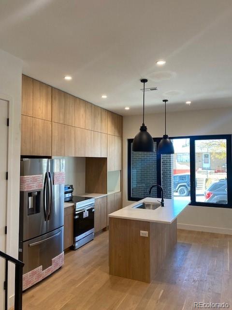 kitchen with appliances with stainless steel finishes, decorative light fixtures, a kitchen island with sink, light countertops, and a sink