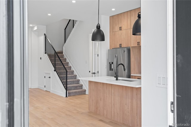 kitchen with a sink, light countertops, stainless steel fridge with ice dispenser, modern cabinets, and pendant lighting