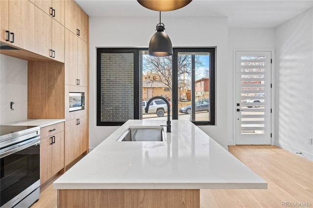 kitchen featuring a kitchen island with sink, a sink, decorative light fixtures, and stainless steel electric stove