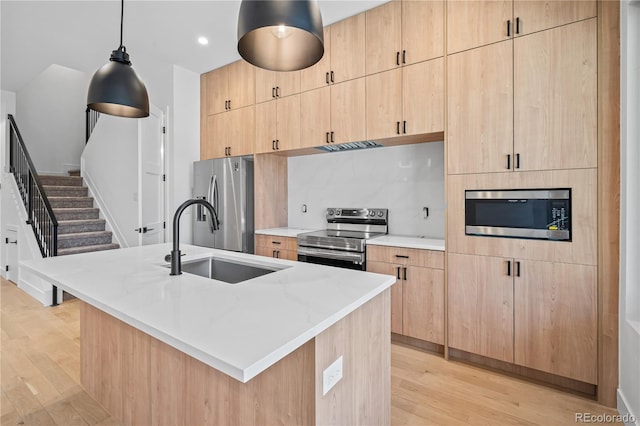 kitchen featuring appliances with stainless steel finishes, light stone counters, a kitchen island with sink, light brown cabinets, and a sink