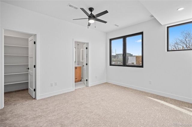 unfurnished bedroom featuring connected bathroom, light carpet, visible vents, baseboards, and a walk in closet