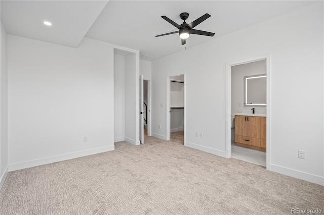 unfurnished bedroom with light carpet, a spacious closet, ensuite bath, and baseboards