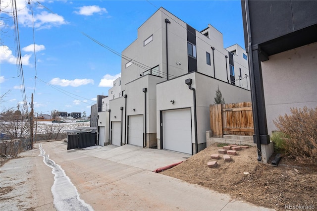 view of property exterior featuring driveway, a residential view, an attached garage, fence, and stucco siding