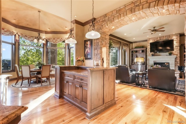 17540 Pond View Pl, Colorado Springs, CO 80908 - kitchen with ornamental molding, light wood-style flooring, ceiling fan, a glass covered fireplace, and hanging light fixtures