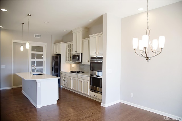 kitchen with tasteful backsplash, hanging light fixtures, a kitchen island with sink, dark hardwood / wood-style floors, and stainless steel appliances