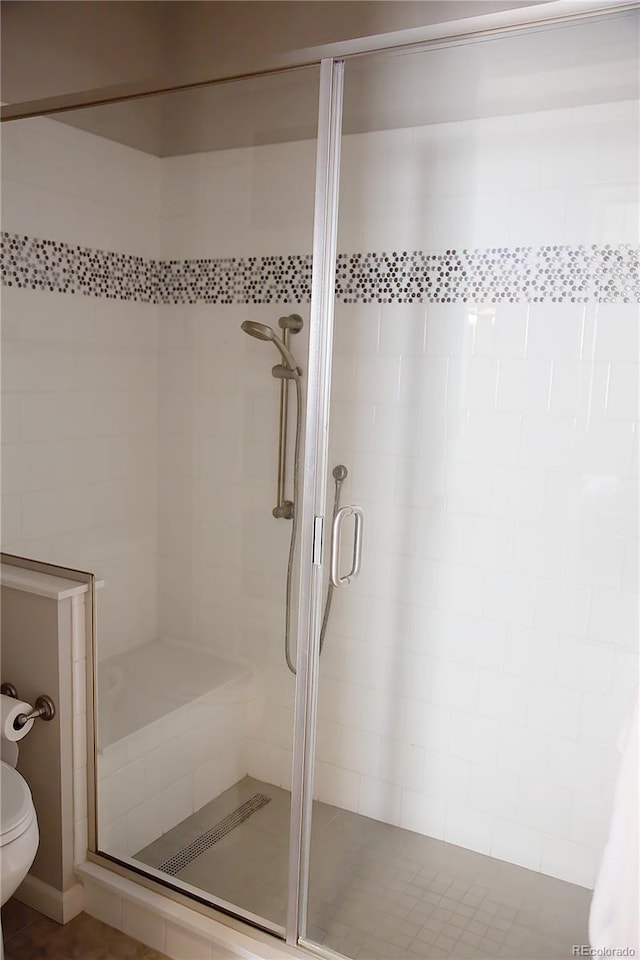 bathroom featuring a shower with door and toilet