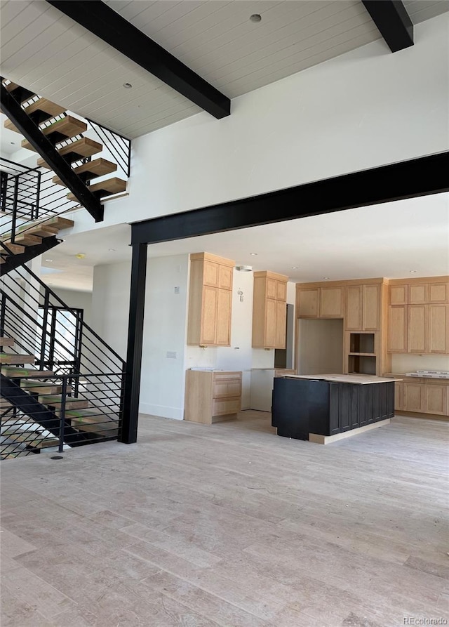 unfurnished living room with beamed ceiling, a towering ceiling, and stairway