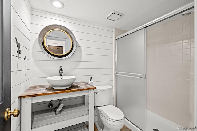 bathroom with wooden walls, vanity, a shower stall, and toilet