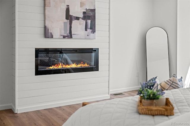 bedroom featuring visible vents, baseboards, wood finished floors, and a glass covered fireplace