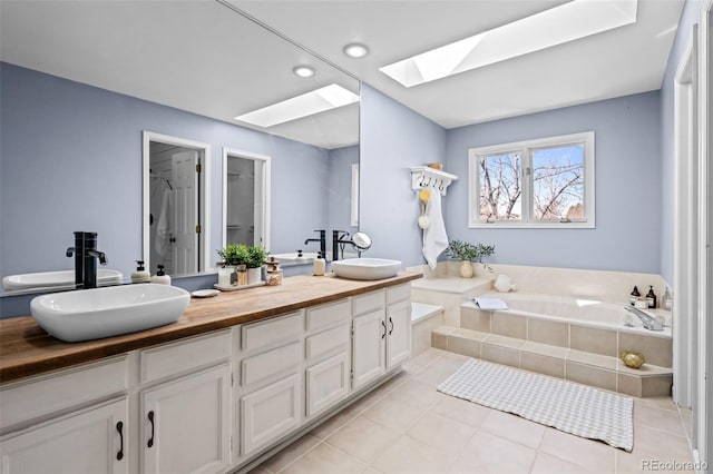 bathroom featuring a garden tub, tile patterned floors, a sink, and a skylight