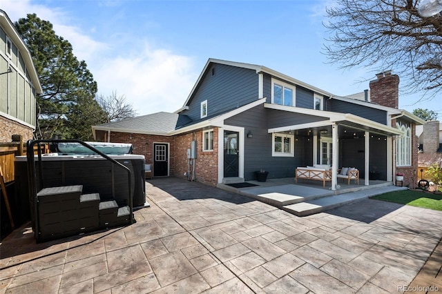 rear view of house featuring outdoor lounge area, a chimney, a patio area, brick siding, and a hot tub