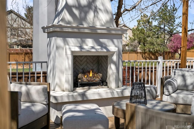 view of patio with fence and a warm lit fireplace