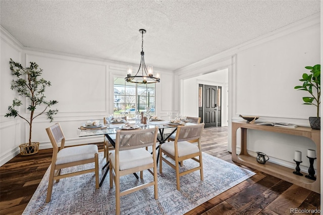 dining room featuring dark wood finished floors, an inviting chandelier, a decorative wall, crown molding, and a textured ceiling