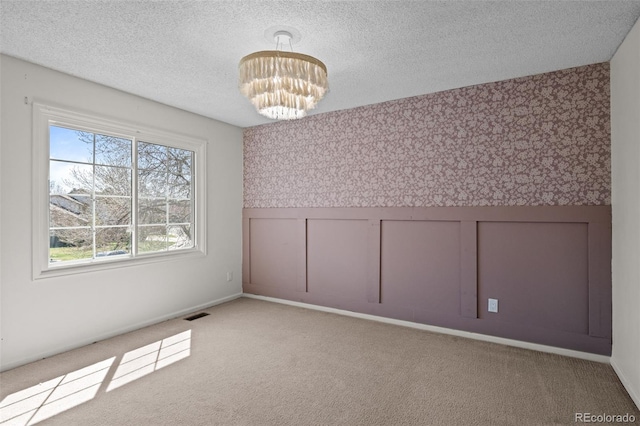 empty room featuring a textured ceiling, visible vents, carpet floors, and a notable chandelier