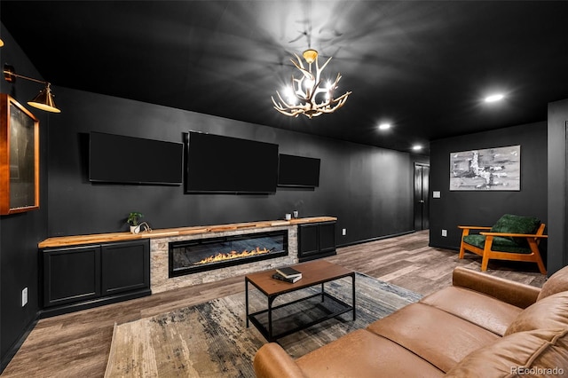 cinema room with recessed lighting, wood finished floors, baseboards, a glass covered fireplace, and a notable chandelier
