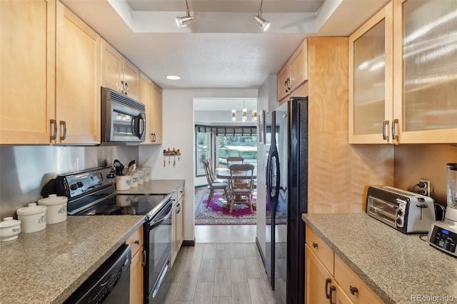 kitchen with light brown cabinetry, light stone countertops, black appliances, and light wood-type flooring