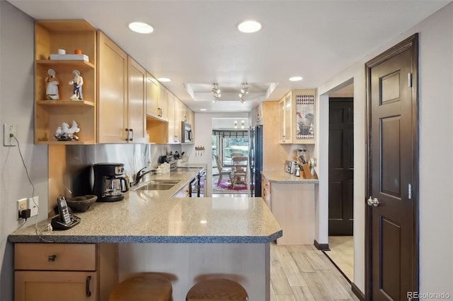 kitchen featuring a breakfast bar, kitchen peninsula, sink, appliances with stainless steel finishes, and light brown cabinets