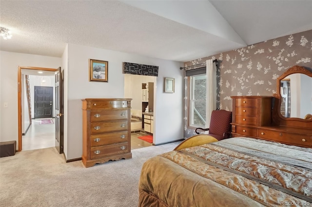 carpeted bedroom featuring vaulted ceiling, a textured ceiling, and ensuite bath