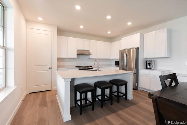 2967 S Quaker St, Morrison, CO 80465 - kitchen featuring stainless steel refrigerator with ice dispenser, under cabinet range hood, light wood-style flooring, a kitchen bar, and white cabinets