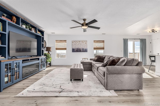 living room featuring ceiling fan, a textured ceiling, and light wood-type flooring