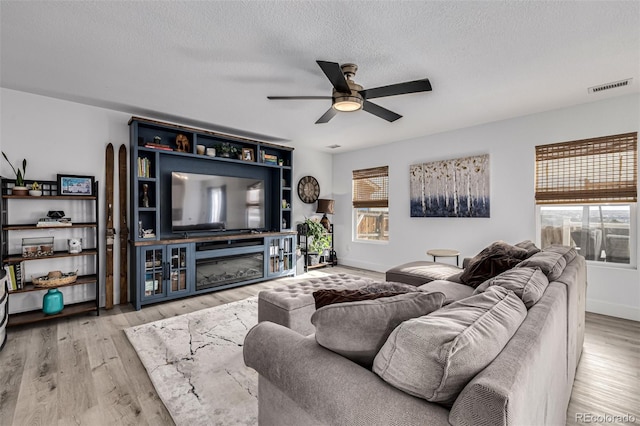 living room featuring a textured ceiling, light wood-type flooring, and ceiling fan