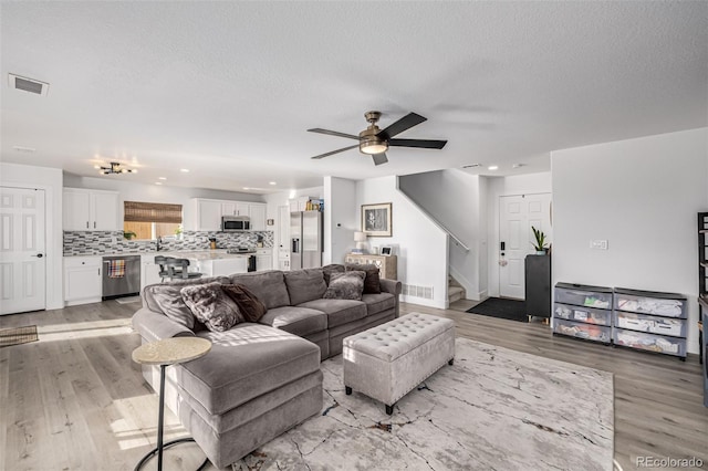 living room with a textured ceiling, light wood-type flooring, ceiling fan, and sink