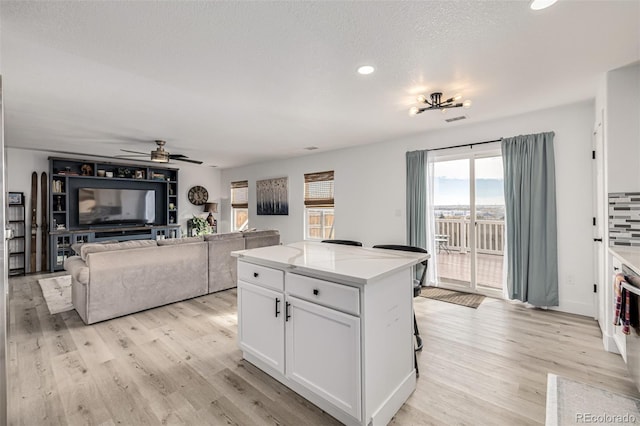 kitchen with a textured ceiling, a kitchen island, ceiling fan, light hardwood / wood-style flooring, and white cabinetry