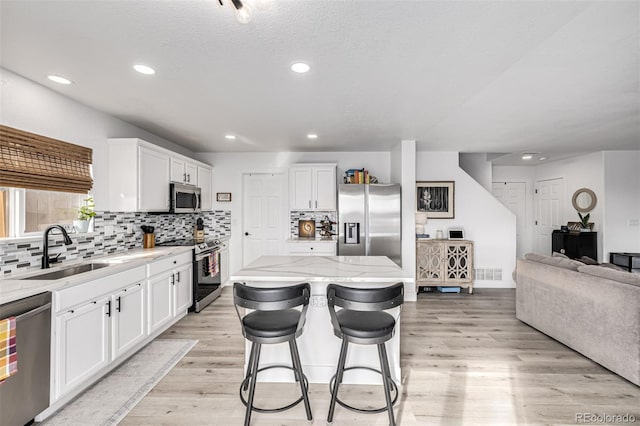 kitchen featuring a center island, stainless steel appliances, light hardwood / wood-style floors, a breakfast bar area, and white cabinets