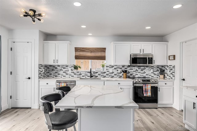 kitchen featuring a center island, sink, appliances with stainless steel finishes, light hardwood / wood-style floors, and white cabinetry