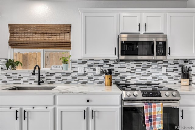 kitchen featuring white cabinets, appliances with stainless steel finishes, light stone countertops, and sink