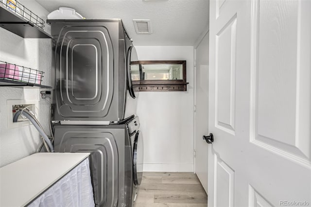 clothes washing area with a textured ceiling, light hardwood / wood-style flooring, and stacked washer and clothes dryer