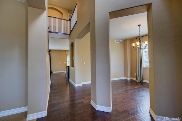 corridor with baseboards, arched walkways, a chandelier, and dark wood-style floors