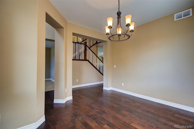 spare room with an inviting chandelier, stairs, wood finished floors, and visible vents