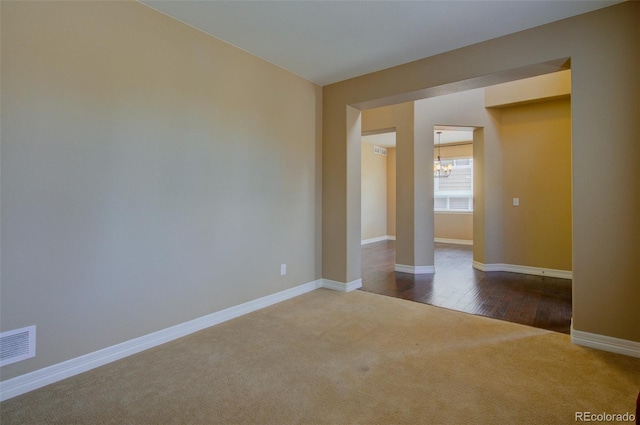unfurnished room with baseboards, a chandelier, dark carpet, and visible vents